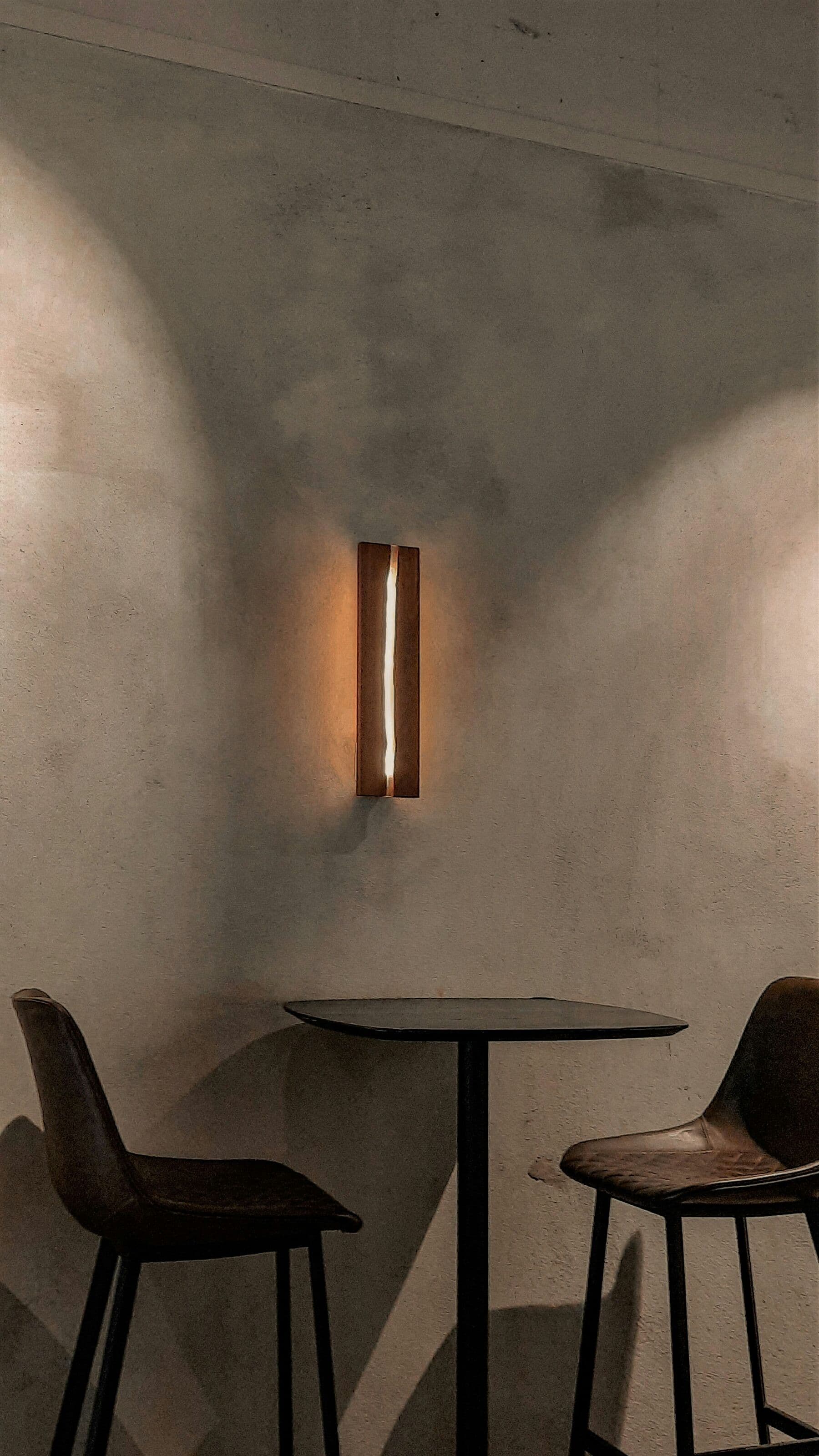 Applique en bois diffusant une lumière chaude sur un mur enduit, au-dessus d'une table haute.