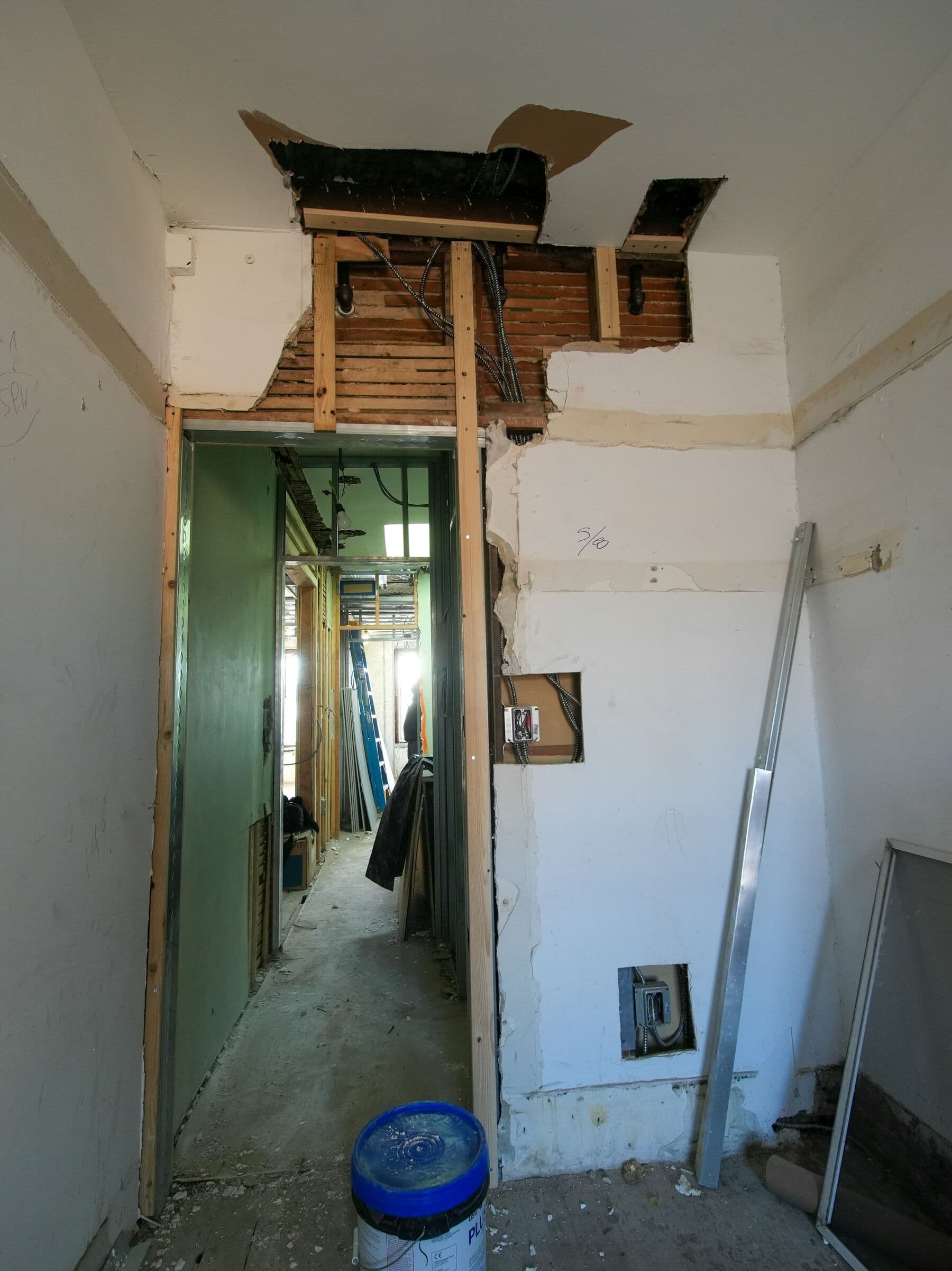 Couloir en chantier : cloisons éventrées, plafond ouvert et gravats au sol.