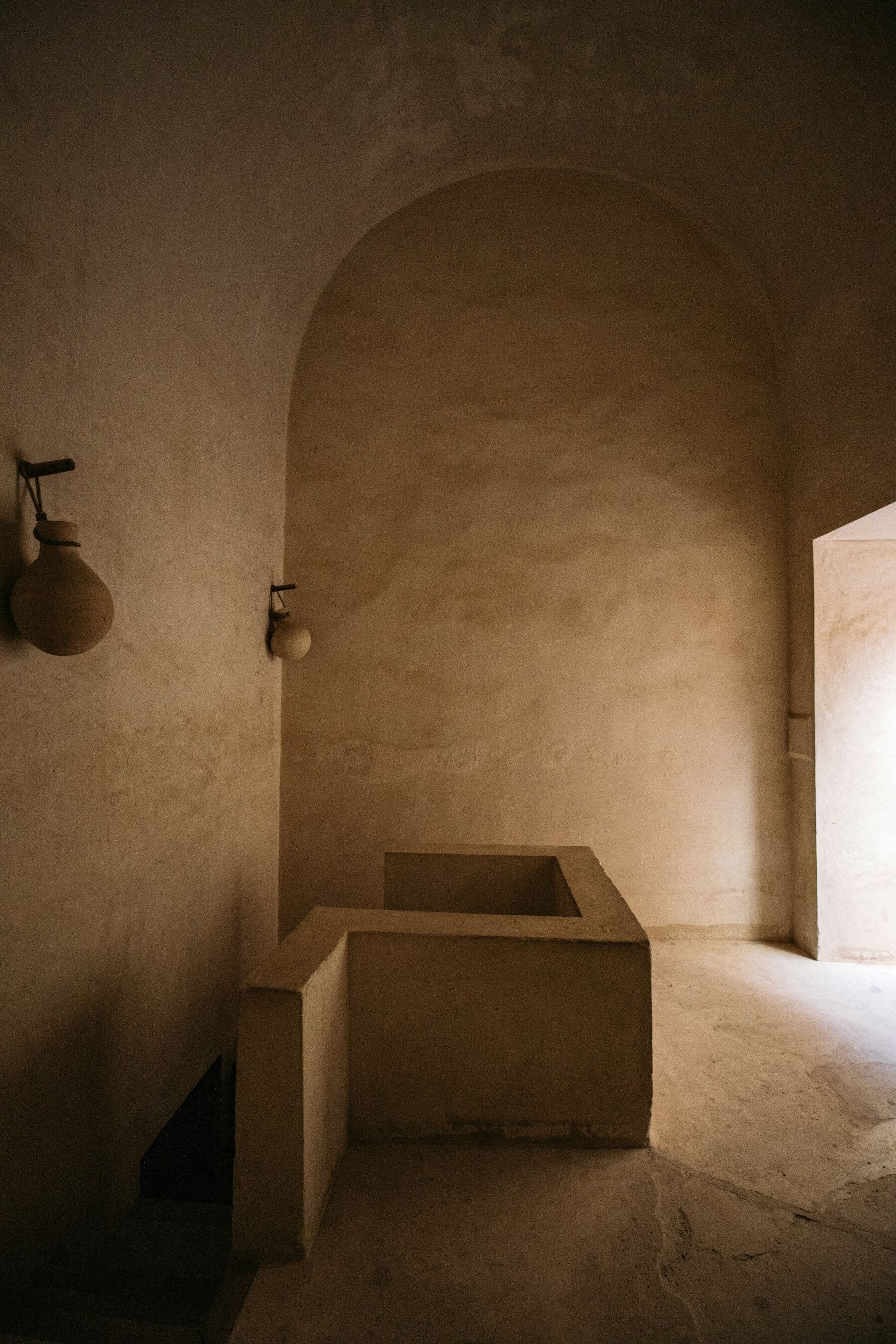 Salle de bain voûtée en tadelakt sable avec une baignoire maçonnée et une lumière chaude.