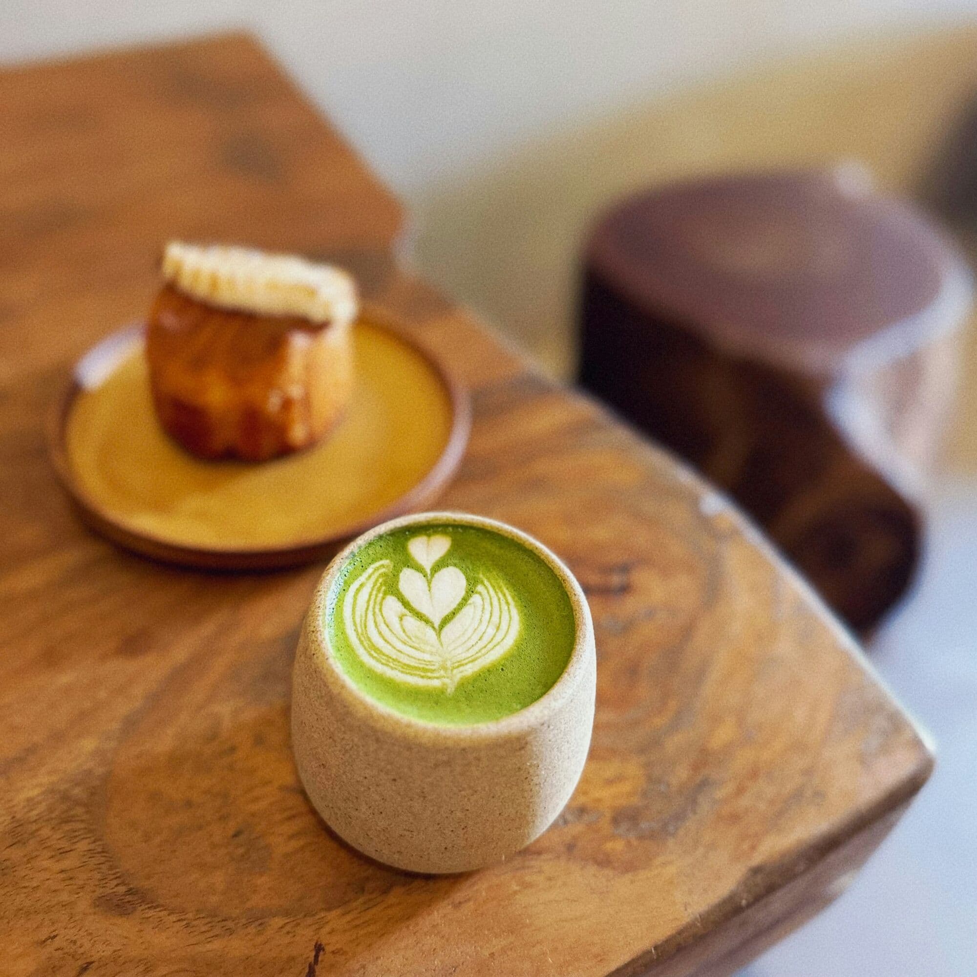 Tasse de thé matcha et canelé posés sur un plateau de bois massif.