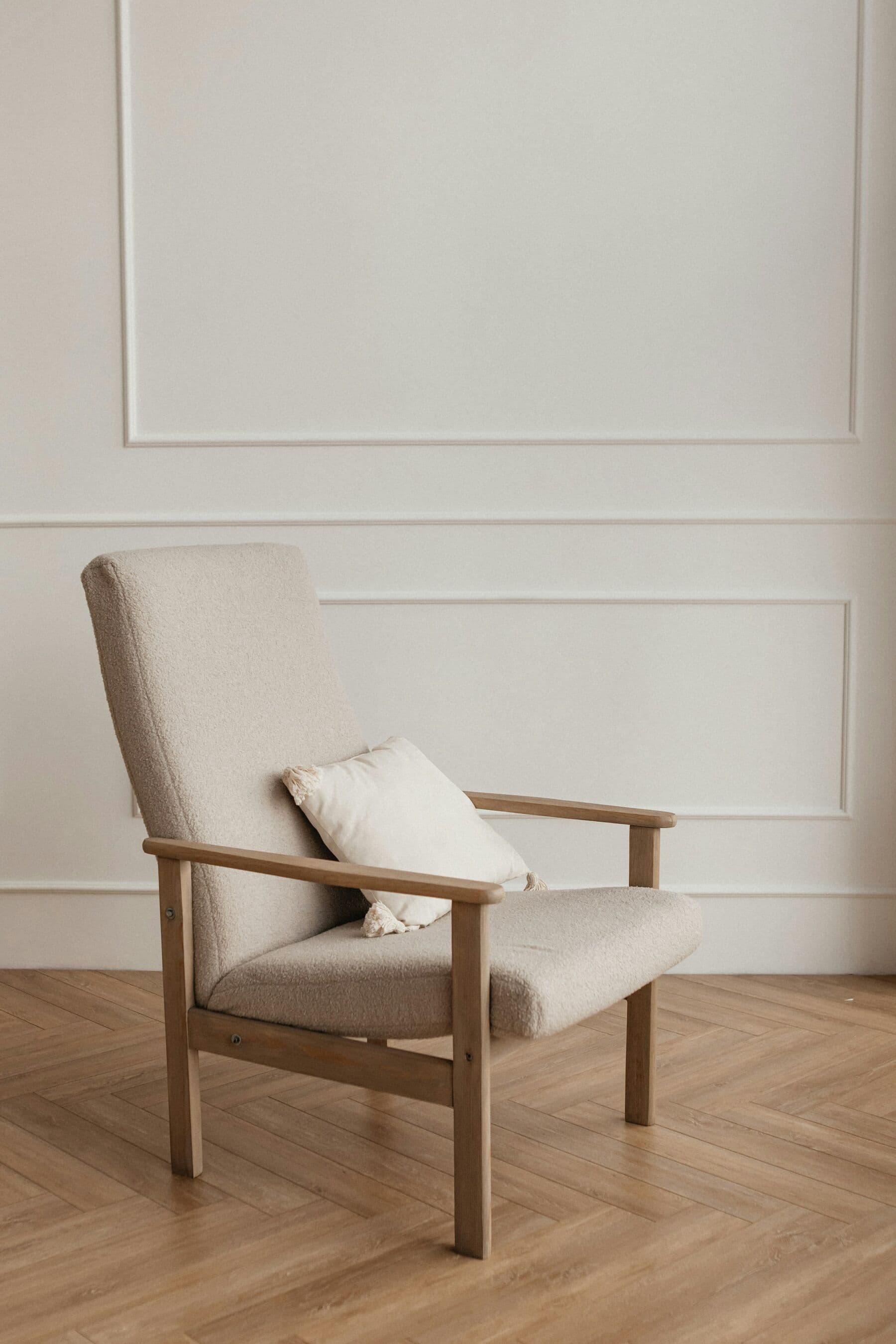 Fauteuil en chêne et lin devant un mur à moulures blanc, sur un parquet en point de Hongrie.