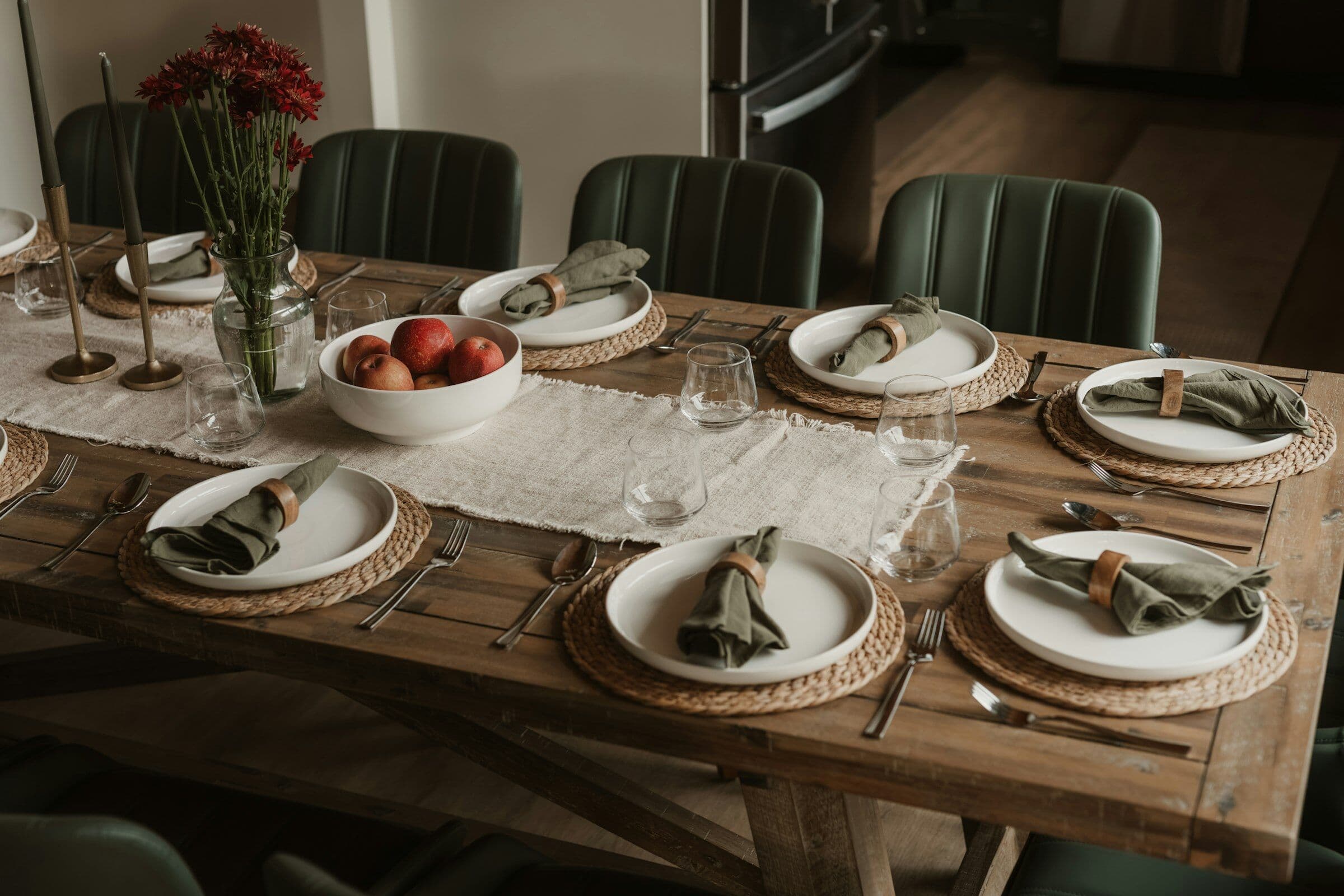 Longue table de bois dressée pour le dîner avec des assiettes de grès, des fruits et des fleurs.