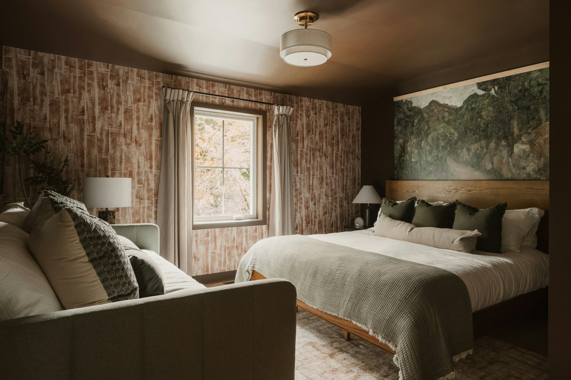 Chambre aux tons bruns avec un lit en bois, une fresque de paysage et un canapé au premier plan.