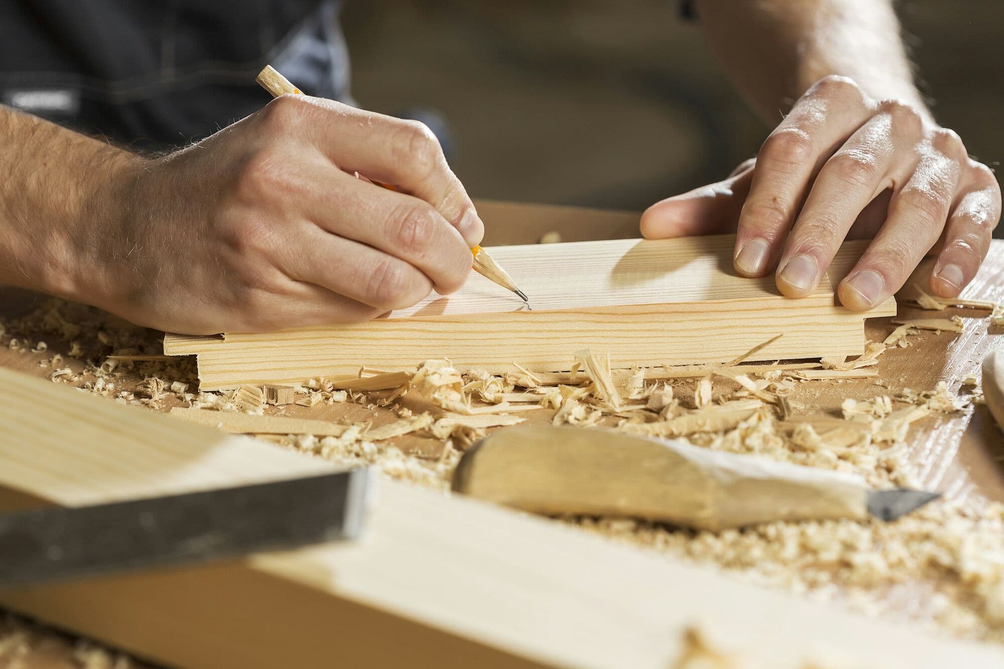 Mains traçant un repère au crayon sur une pièce de bois, parmi les copeaux.