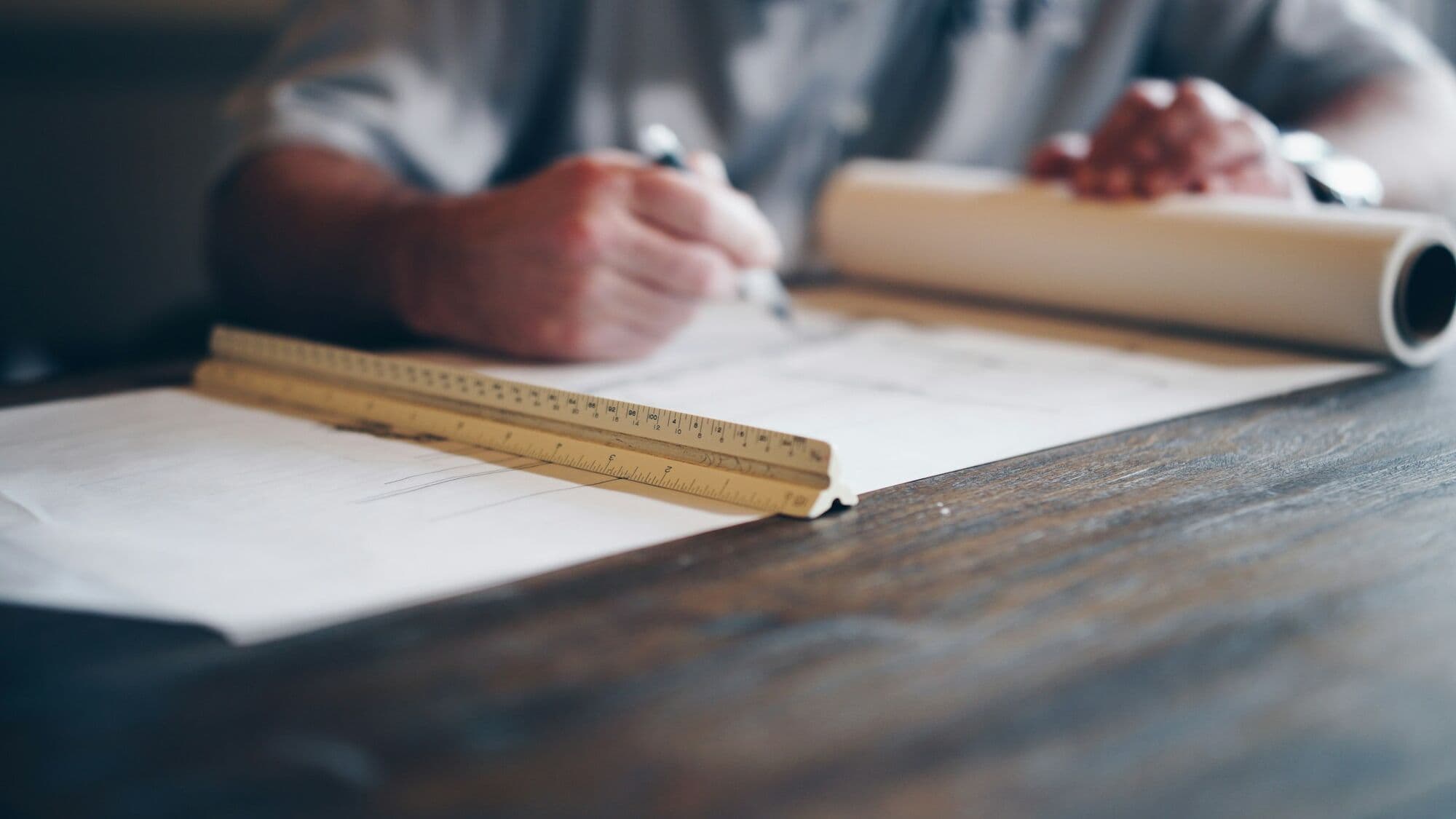 Mains traçant un plan à la règle sur une table de bois sombre.
